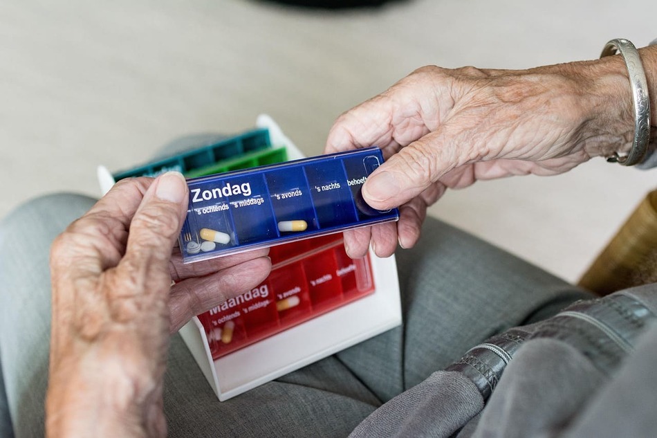Primer plano de las manos de una persona mayor sosteniendo un organizador de pastillas azul con divisiones para diferentes momentos del día.