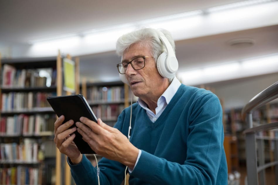 Un hombre mayor sonriendo con auriculares inalámbricos mientras descansa en un sofá de cuero.