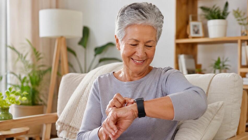 Persona mayor sonriendo mientras revisa un reloj inteligente en una sala luminosa con elementos de madera.